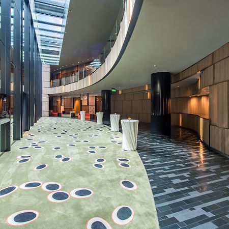 Crowne Plaza Changi Airport By Ihg Сингапур Экстерьер фото The photo shows a modern indoor space that features a curved hallway with a mix of materials and textures. The floor is divided into two sections: one has a smooth, dark tiled design, while the other has a soft, green carpet with circular patterns in