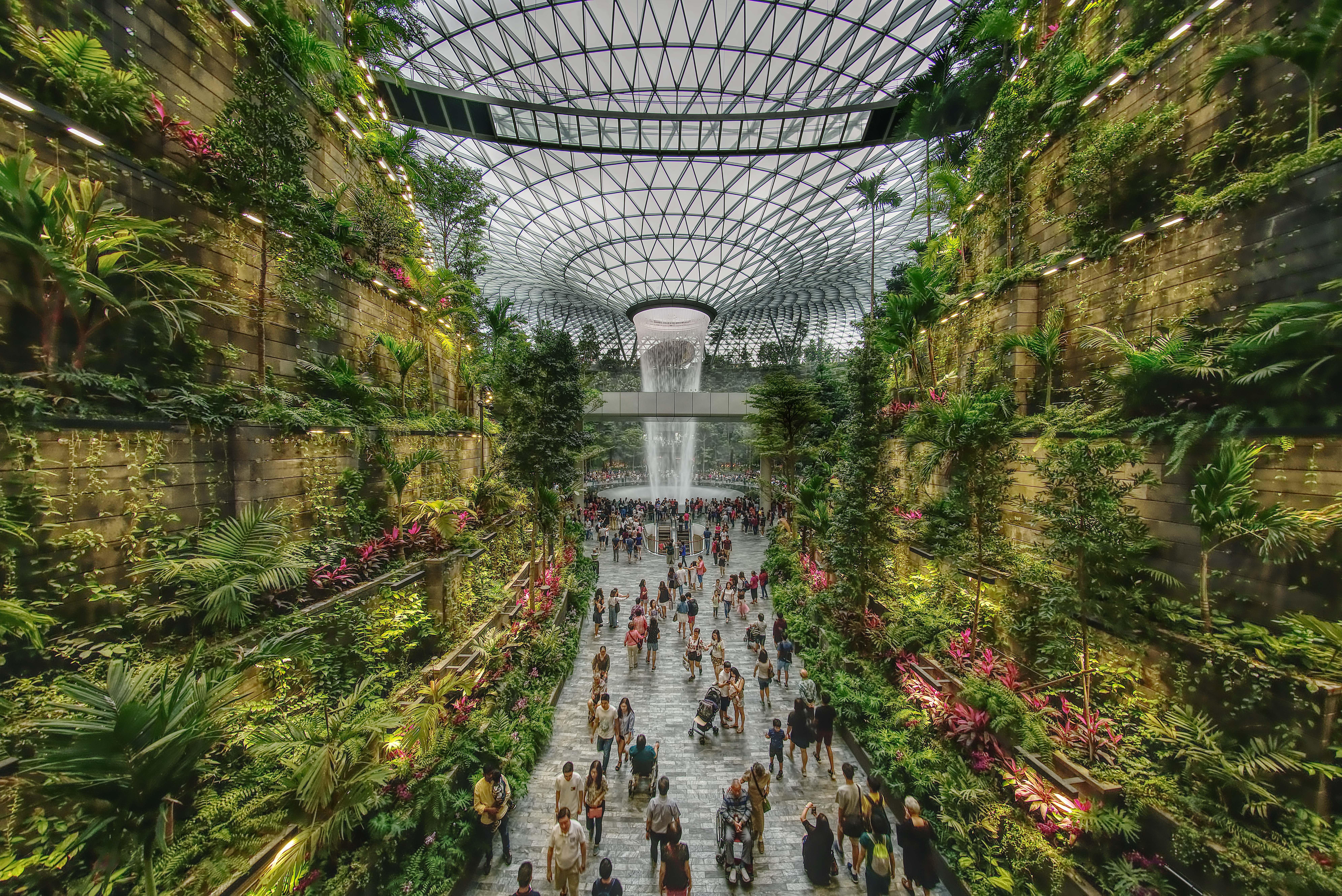 Crowne Plaza Changi Airport By Ihg Сингапур Экстерьер фото The photo depicts a vibrant indoor garden space, characterized by lush greenery and a towering waterfall at its center. The setting features vertical gardens on stone walls, filled with various plants and flowers. People can be seen walking along the