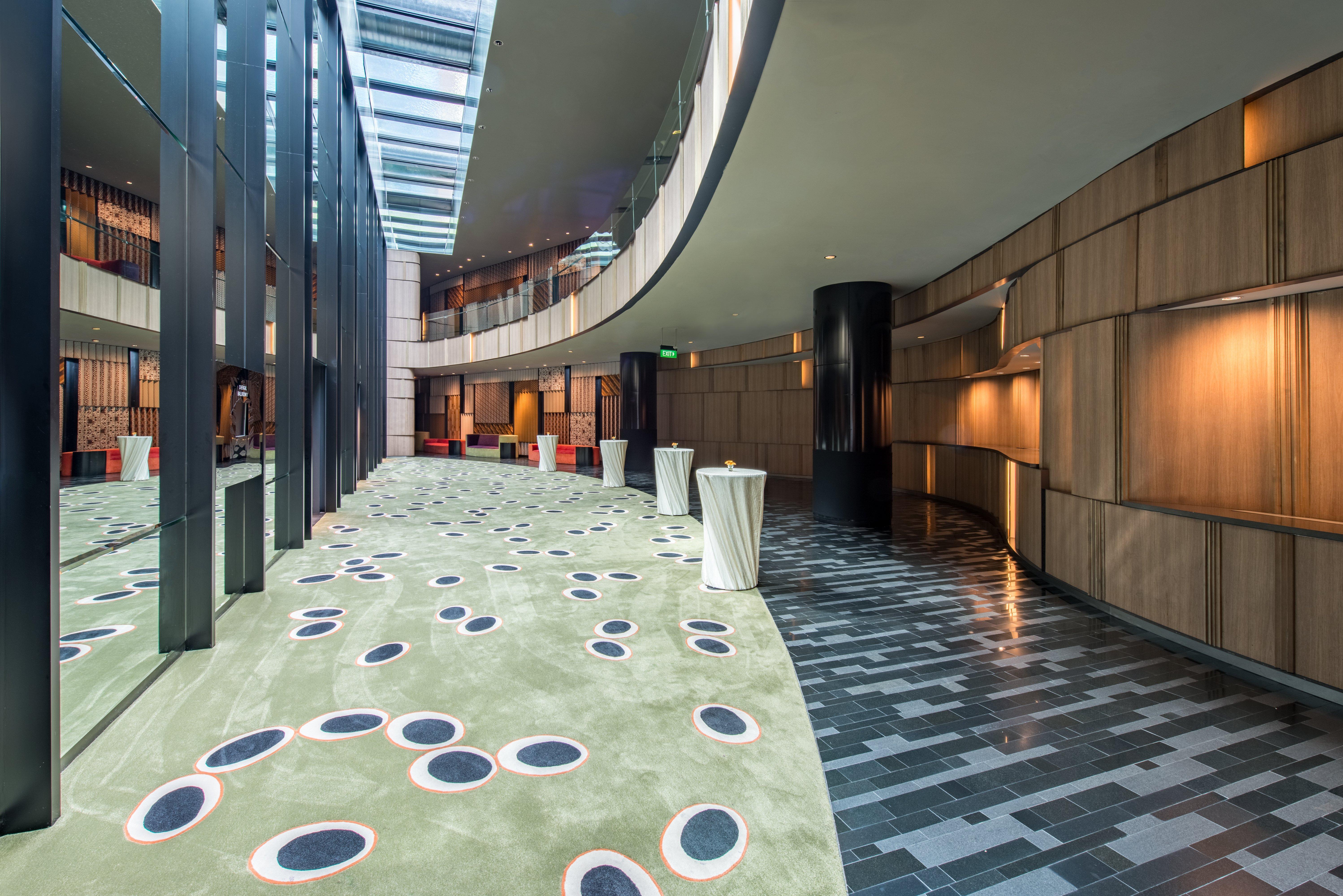 Crowne Plaza Changi Airport By Ihg Сингапур Экстерьер фото The photo shows a modern indoor space that features a curved hallway with a mix of materials and textures. The floor is divided into two sections: one has a smooth, dark tiled design, while the other has a soft, green carpet with circular patterns in