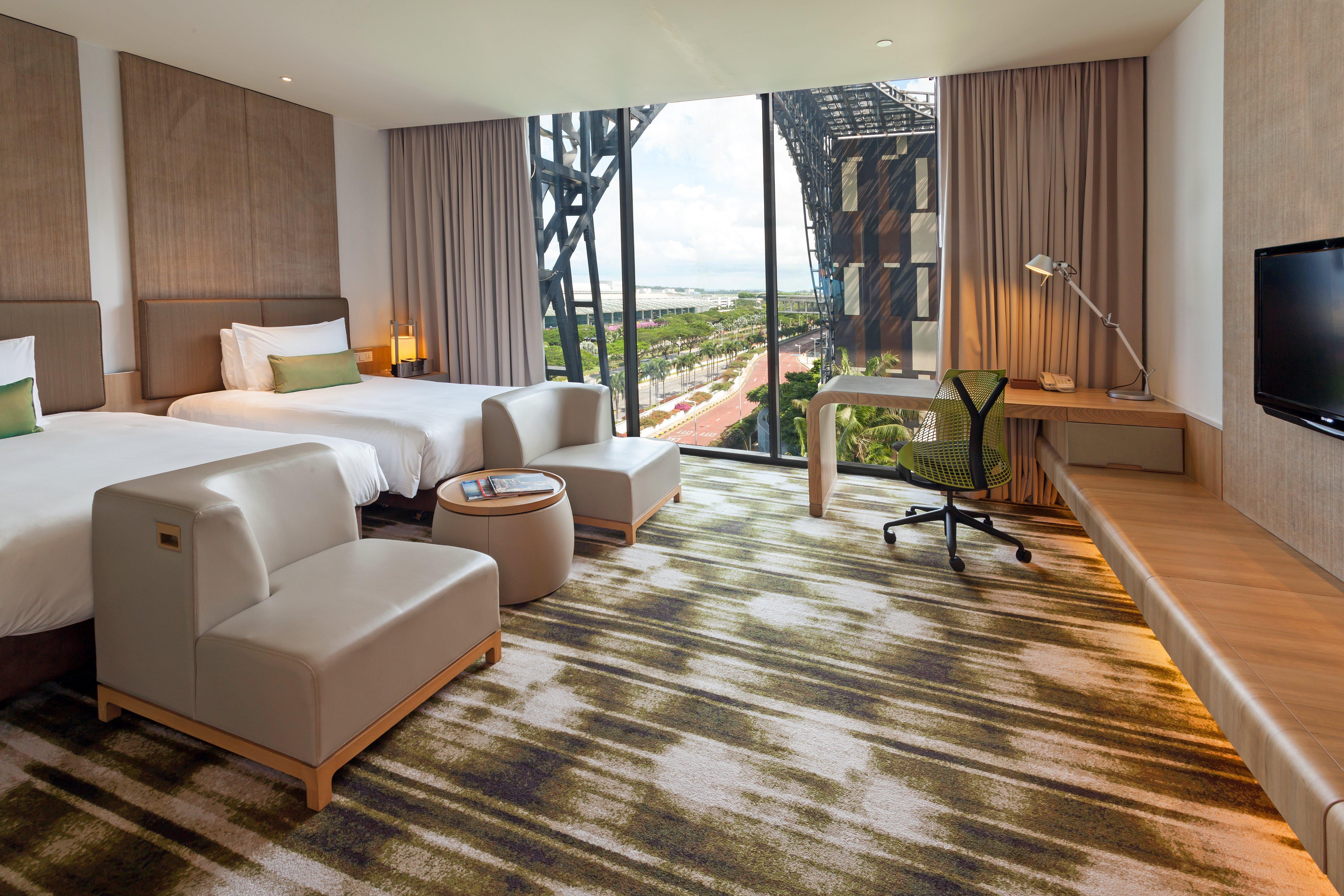 Crowne Plaza Changi Airport By Ihg Сингапур Экстерьер фото The photo depicts a modern hotel room featuring two beds with white linens and a clean, minimalist design. There are two stylish armchairs and a small round table, creating a cozy seating area. The room includes a large window that offers a view of t