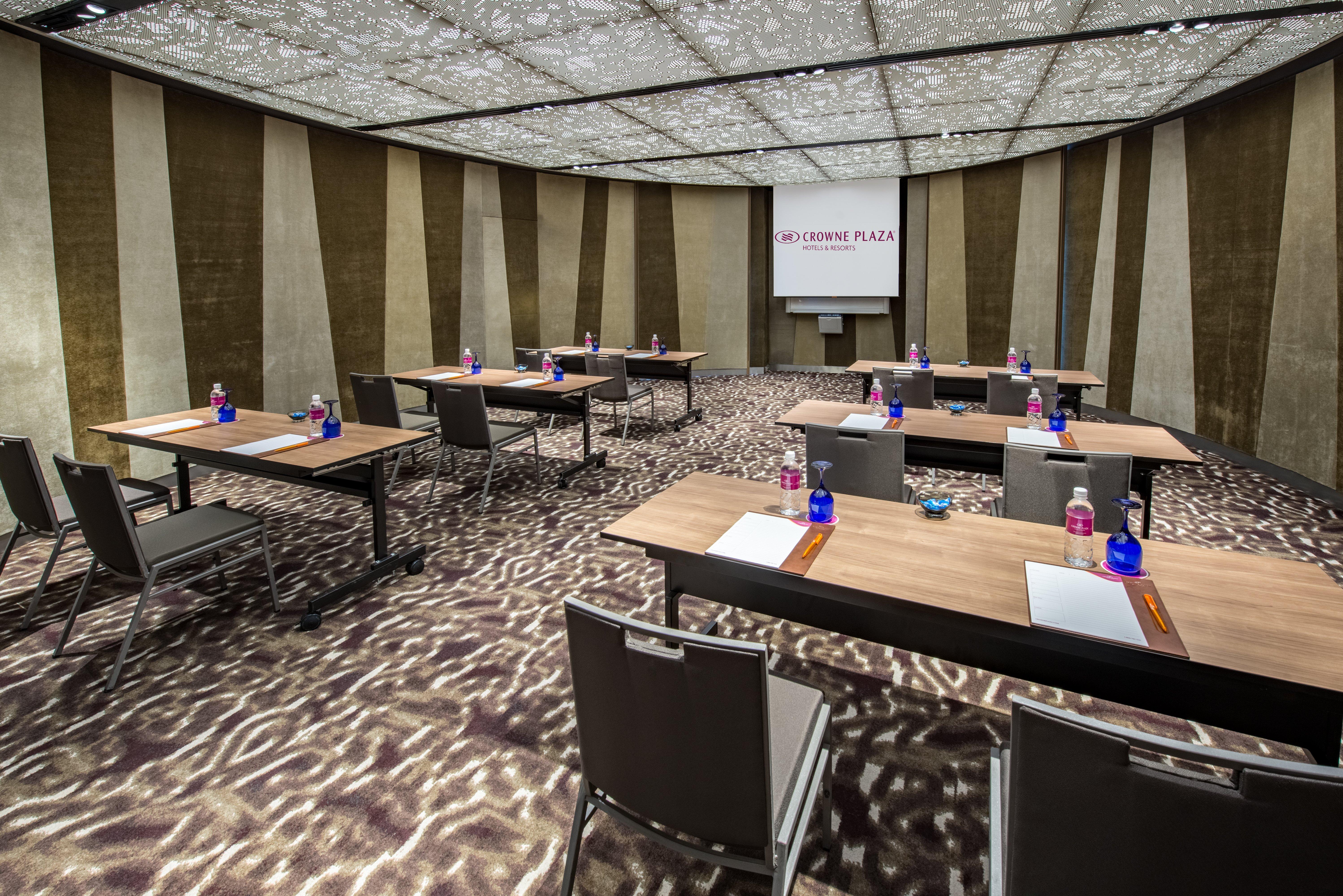 Crowne Plaza Changi Airport By Ihg Сингапур Экстерьер фото The photo shows a modern conference room set up for a meeting or presentation. There are several wooden tables arranged in a U-shape, each equipped with a notepad and pen. Bottled water is placed in blue containers on the tables. The room features a 
