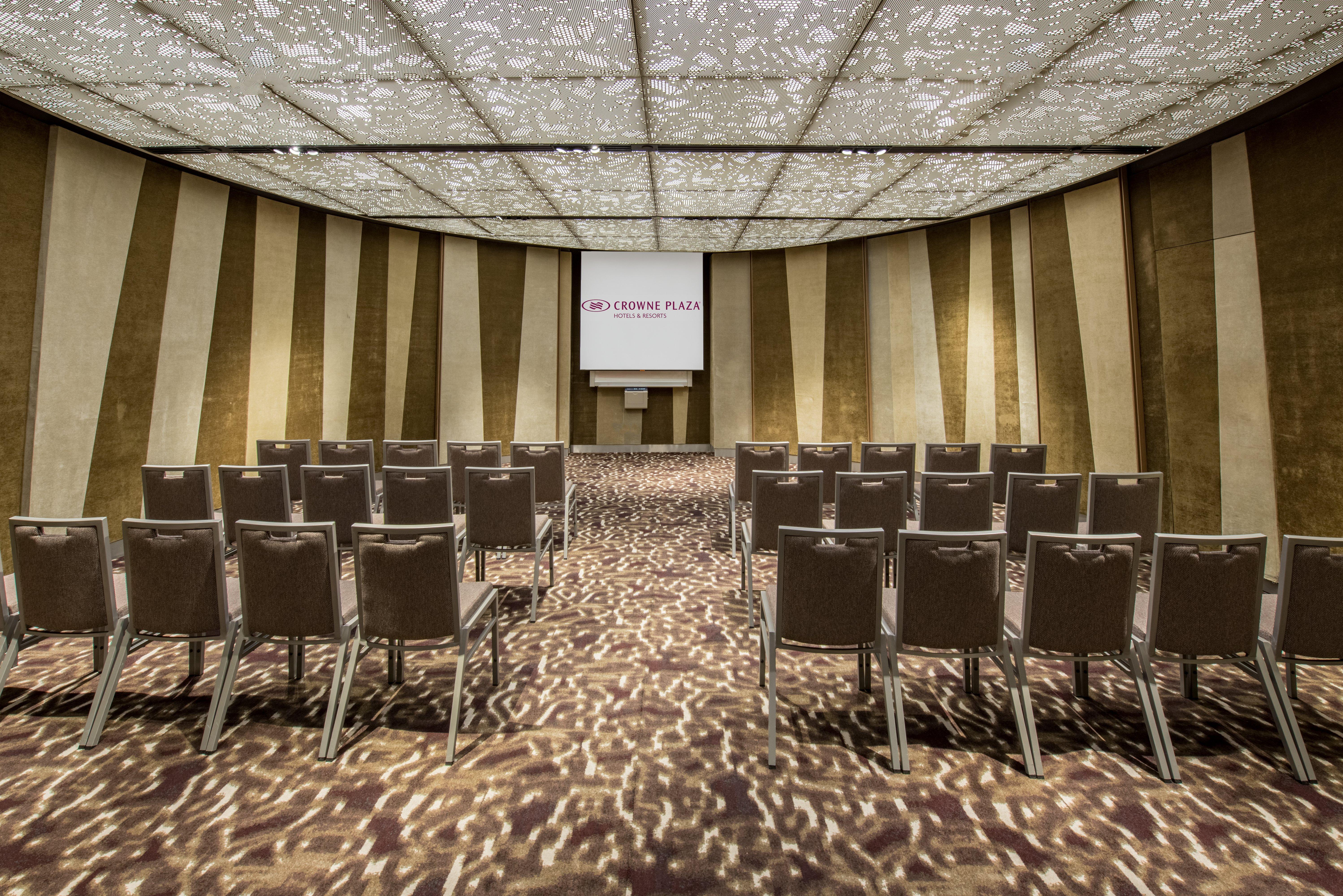 Crowne Plaza Changi Airport By Ihg Сингапур Экстерьер фото The photo shows a conference or meeting room. It features rows of grey chairs arranged in a semi-circular layout, facing a screen at the front. The room has a decorative ceiling with a patterned design that allows light to filter through, creating in