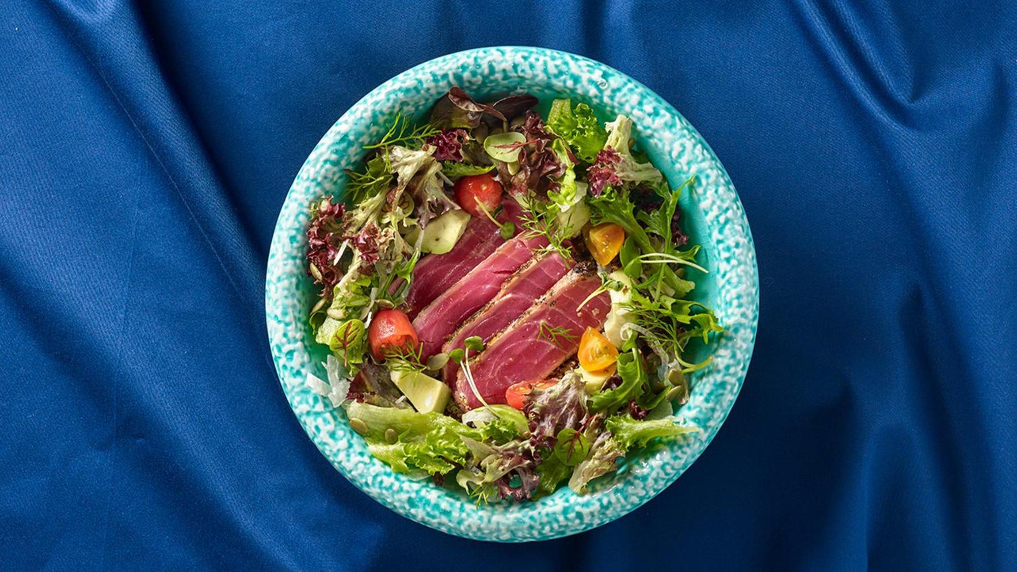 Crowne Plaza Changi Airport By Ihg Сингапур Экстерьер фото The photo shows a bowl of salad featuring a variety of fresh leafy greens, including different types of lettuce. There are sliced pieces of seared tuna placed over the salad, adding a protein element. The salad is garnished with cherry tomatoes and p