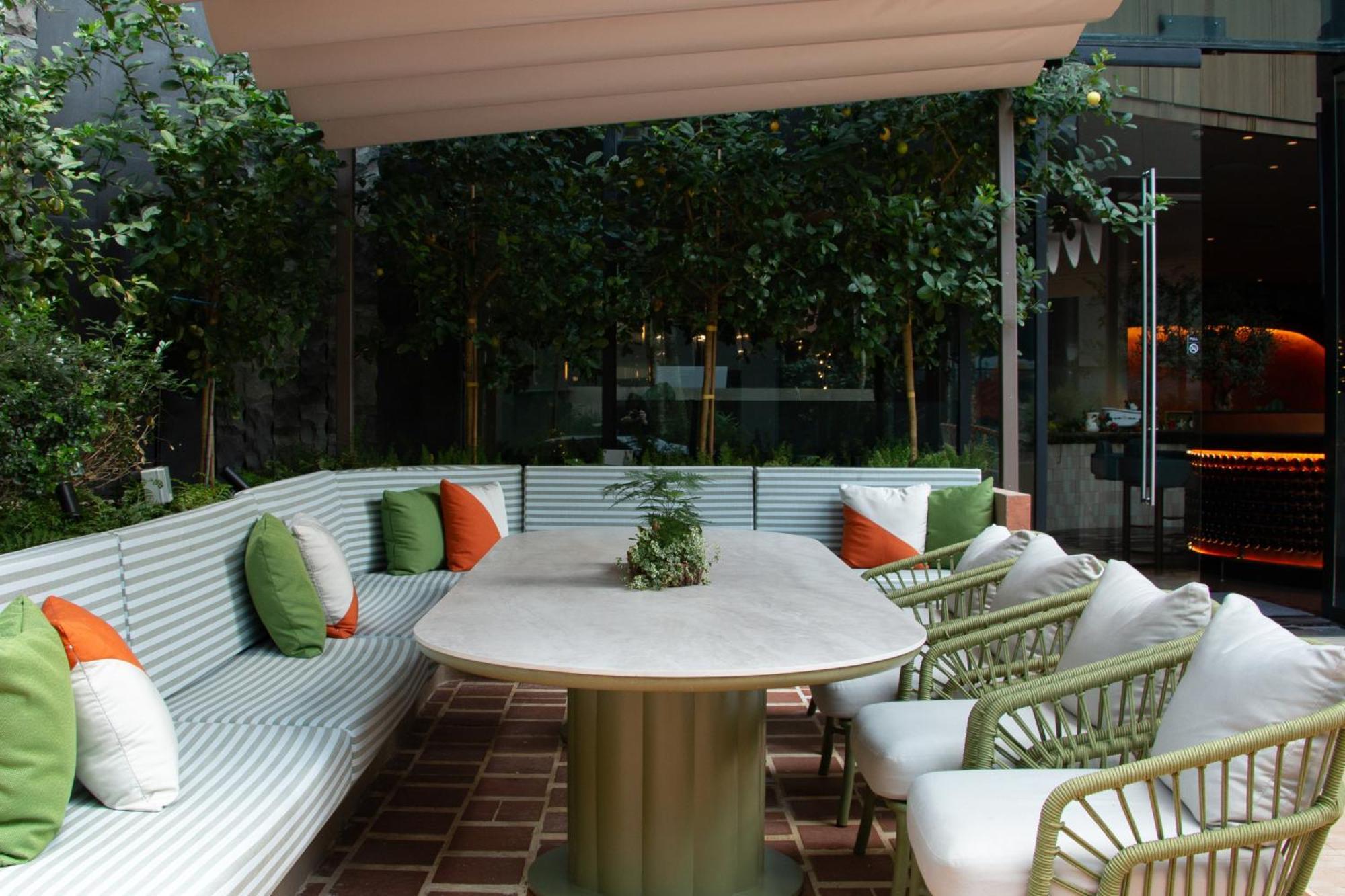 Crowne Plaza Changi Airport By Ihg Сингапур Экстерьер фото The photo shows a stylish outdoor seating area. There is a large, oval table at the center, surrounded by comfortable chairs with white cushions. The seating features a long, curved bench with a light green and white striped design, and it is adorned