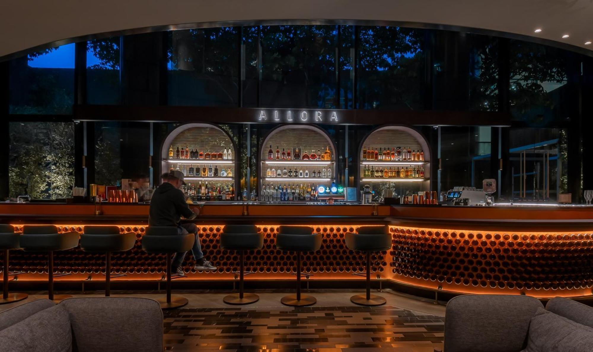 Crowne Plaza Changi Airport By Ihg Сингапур Экстерьер фото The photo shows a bar area with a modern and stylish design. In the center, there is a well-lit bar counter featuring a variety of alcoholic beverages displayed on shelves behind it. The bar has a sleek, contemporary look with circular light fixtures