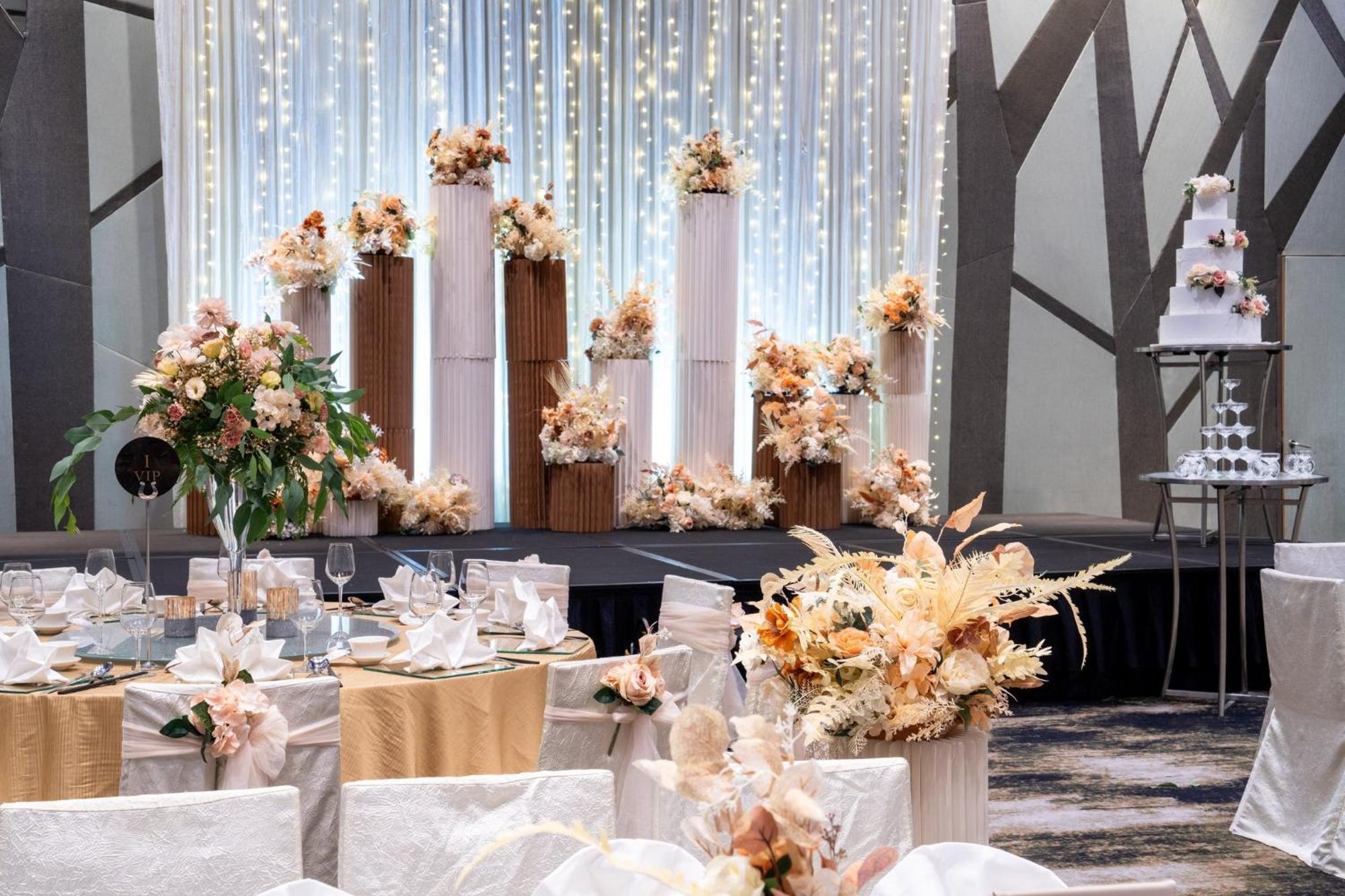 Crowne Plaza Changi Airport By Ihg Сингапур Экстерьер фото The photo shows an elegantly decorated wedding reception. In the background, there are tall columns adorned with floral arrangements in soft, pastel colors. These floral displays are complemented by string lights hanging above, creating a romantic am