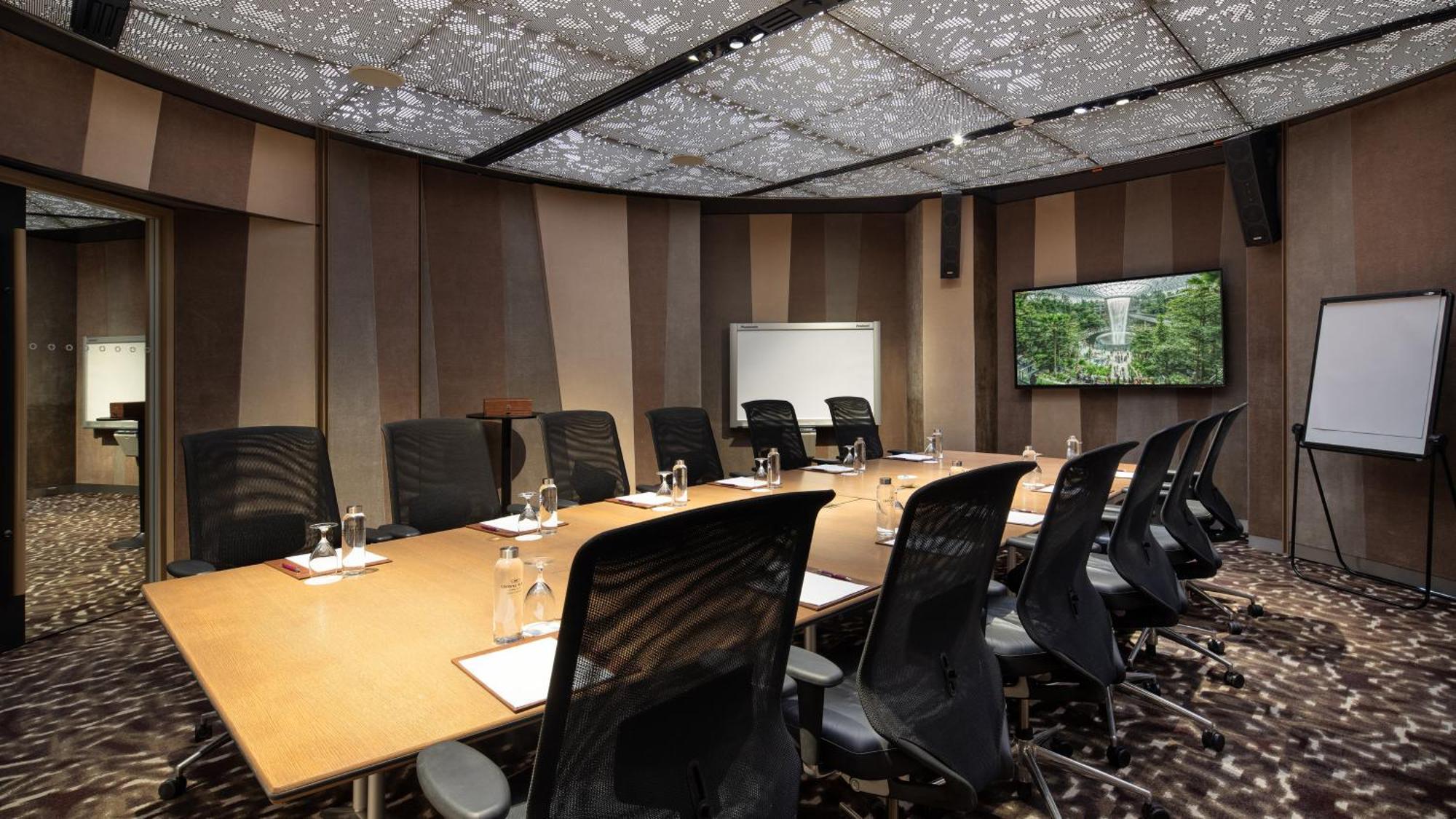 Crowne Plaza Changi Airport By Ihg Сингапур Экстерьер фото The image shows a modern conference room. It features a large rectangular table surrounded by black ergonomic chairs. On the table, there are glasses of water, notepads, and pens. The walls have a sleek design with alternating patterns in neutral col